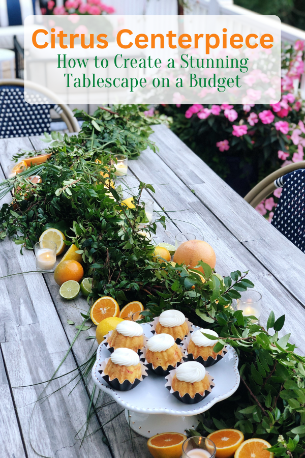 An outdoor citrus tablescape featuring a vibrant citrus centerpiece with fresh oranges, grapefruits, limes, and greenery arranged along the table. The natural wood table is surrounded by navy and white bistro chairs, with colorful flowers and lush greenery in the background. Text overlays the image and reads "Citrus Centerpiece - How to Create a Stunning Tablescape on a Budget"