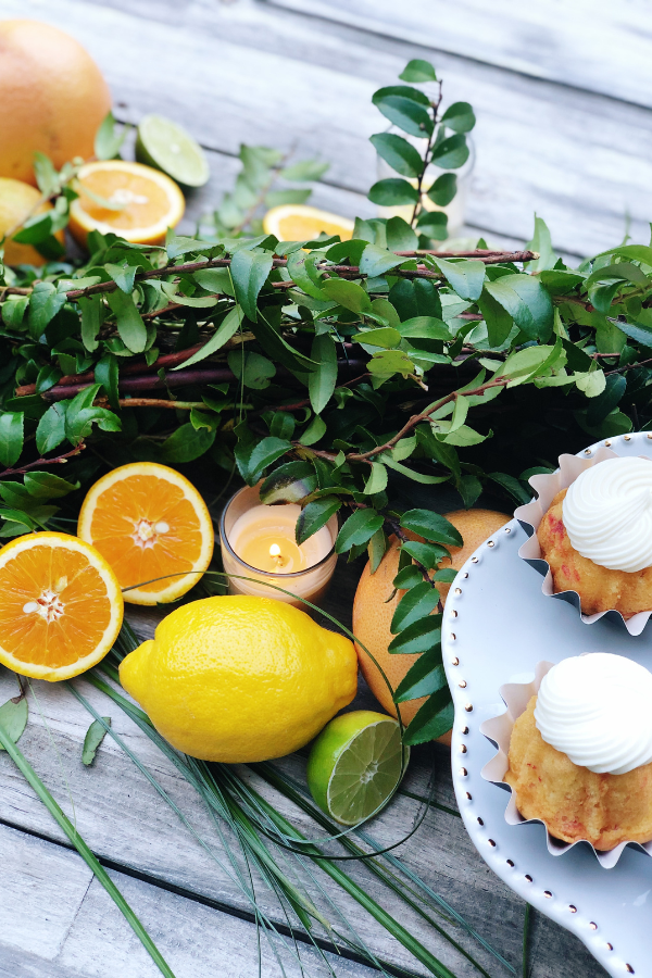 A vibrant lemon nestled in fresh greenery, with halved oranges and limes, beautifully arranged along a rustic wooden table ready to be used as little cutie baby shower decor.

