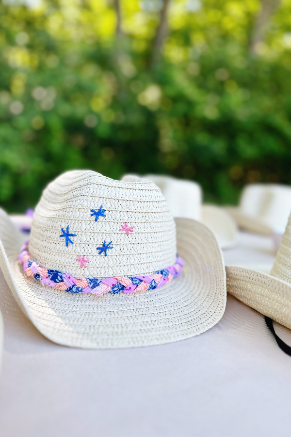 A close-up of a beautifully decorated straw cowboy hat, featuring hand-stitched stars and braided fabric trim. This project is perfect for a cowgirl party, cowgirl bachelorette, or a coastal cowgirl activity. The design blends a vintage cowgirl vibe with a straw hat aesthetic.