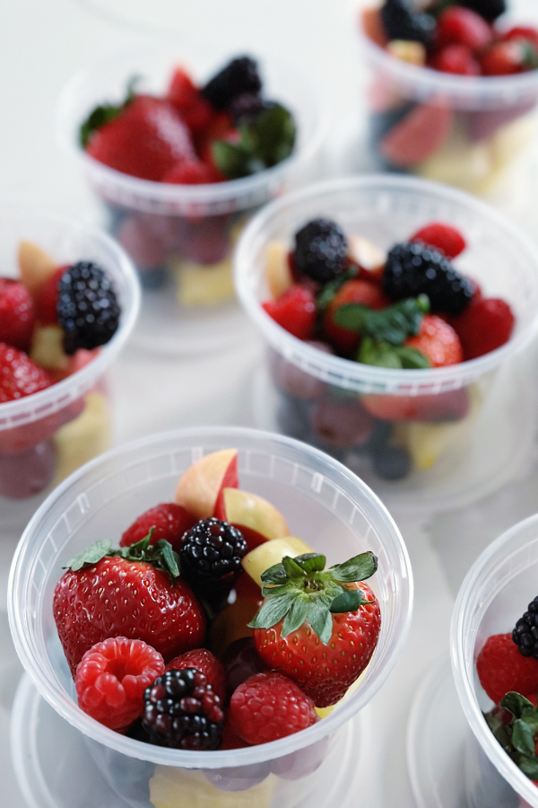 Clear plastic cups filled with a vibrant mix of fresh fruits, including strawberries, raspberries, grapes, and small apple slices, beautiful  presented for individual servings perfect for a picnic snack.