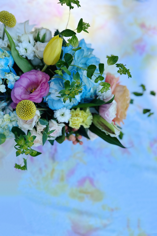 A vibrant floral centerpiece sets the cowgirl bridal shower color palette. Featuring soft blue hydrangeas, peach and pink roses, and yellow tulips, resting on a pastel watercolor quilt background. This elegant arrangement is perfect for a country bridal shower or boho western cowgirl wedding, complementing a cowgirl bachelorette party decoration with a touch of rustic charm.