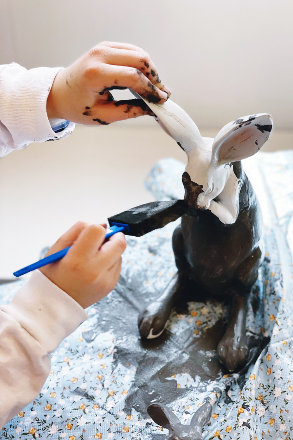 A child painting a Easter bunny craft with dark charcoal gray paint using a foam brush. This easy Easter craft for kids transforms Dollar Tree DIY crafts into stylish Easter home decor. The project is part of a fun Easter craft idea, perfect for homemade Easter decorations or Easter table decorations.