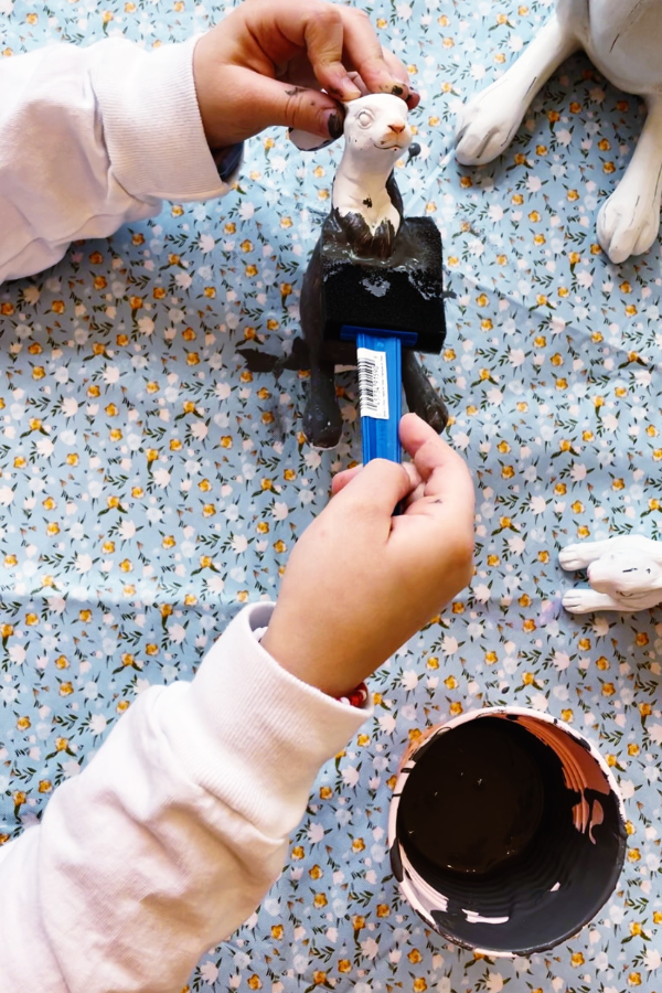 A child using a blue foam brush to paint a small Easter bunny craft, turning it into a cute Easter craft that fits beautifully into Easter home decor. This easy Easter decorations DIY project is perfect for spring Easter crafts, Easter craft projects, or Easter craft decorations made old Easter bunnies or inexpensive new ones.