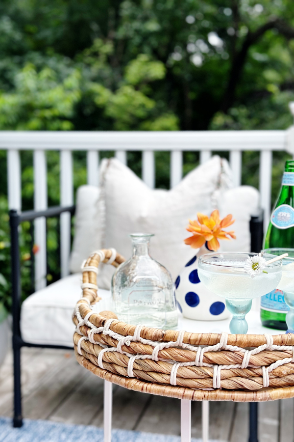 A beautifully styled drink station featuring popsicle cocktails with melting lime popsicles in margarita glasses, garnished with tiny white flowers. The tray also holds a blue polka dot vase with an orange dahlia, a bottle of tequila, and a cork, setting the scene for recipes for entertaining.