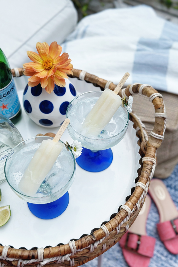 A top-down view of a ranch water recipe in the making, with two margarita glasses filled with ice and boozy popsicles. A sliced lime and a bottle of tequila sit beside the drinks, ready to mix the perfect sparkling water cocktail.