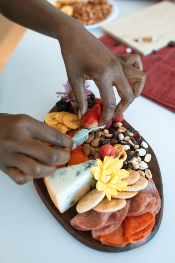 A women at a bridal shower set up building a mini charcuterie board with cheese, crackers, salami, nuts, fruits, and a yellow flower.