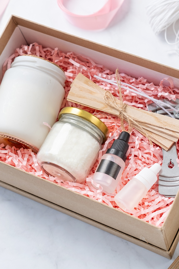 A beautifully packaged brown box with pink crinkle paper and and the essentials for making your own candle for the perfect wedding gifts for guests at a bride shower.